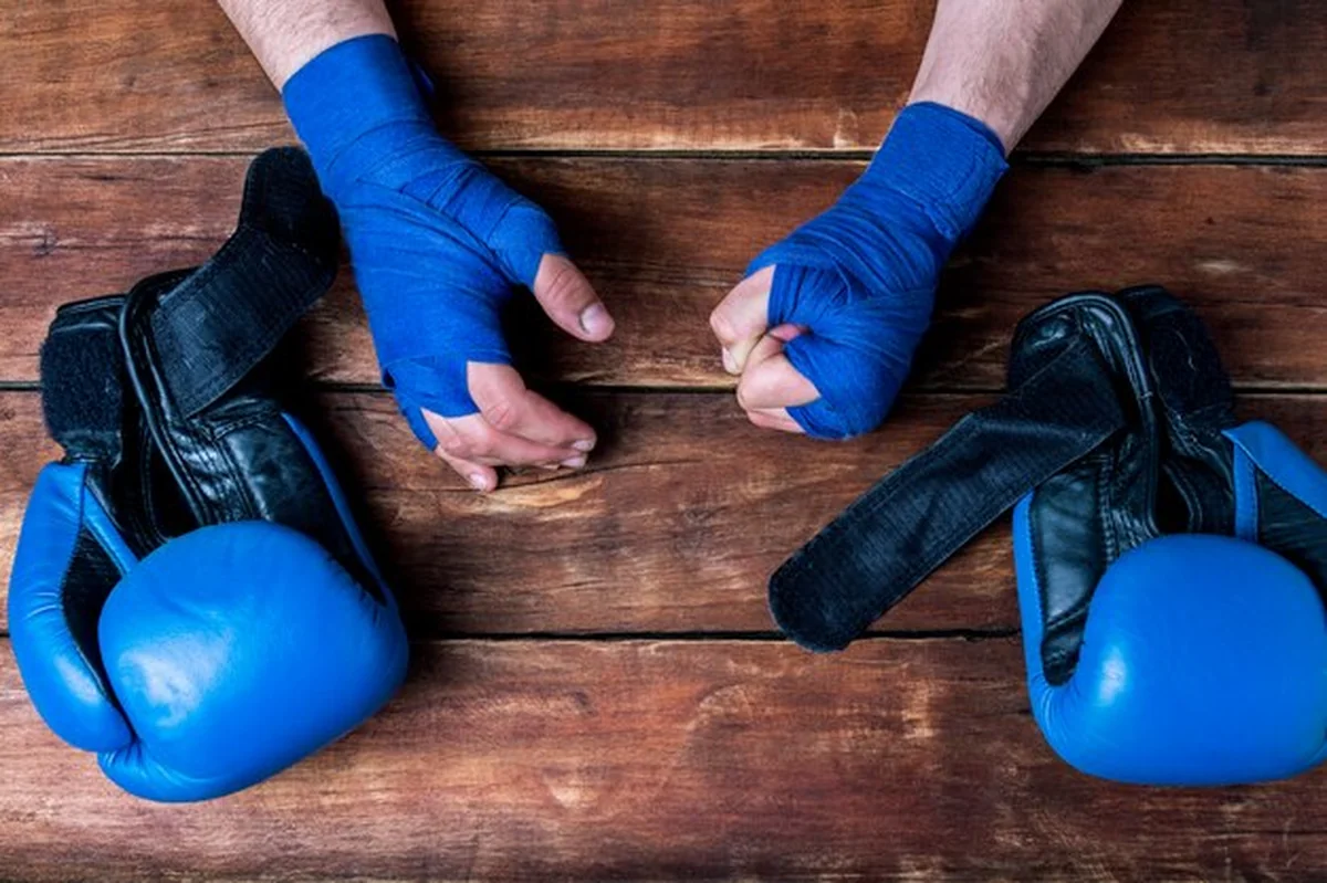 Męskie dłonie w boks bandażach i rękawicach bokserskich na drewnianym tle