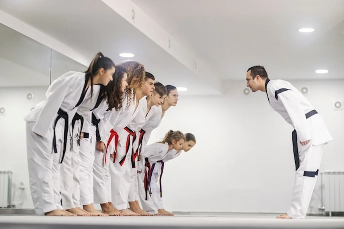 Dzieci taekwondo kłaniają się trenerowi w szkole sztuk walki