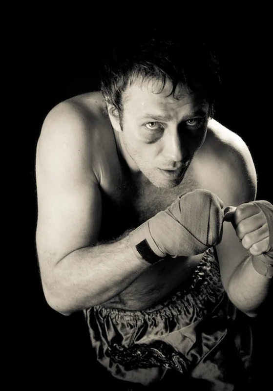 Bokser z podbitym okiem w pozycji bojowej. Zaciśnięte pięści. Ciemne tło